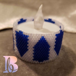 May include: A white and blue beaded candle holder with a white LED tea light inside. The candle holder is decorated with a repeating pattern of blue triangles.