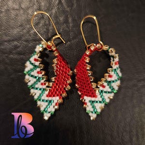 May include: A pair of handmade beaded earrings with a festive design. The earrings feature a teardrop shape with red, white, and green beads, accented with gold-colored beads. The earrings have gold-colored ear wires.