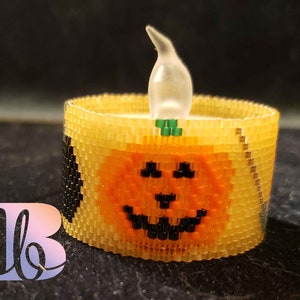 May include: A beaded candle holder shaped like a pumpkin with a black and orange face. The candle holder has a clear plastic flame on top.