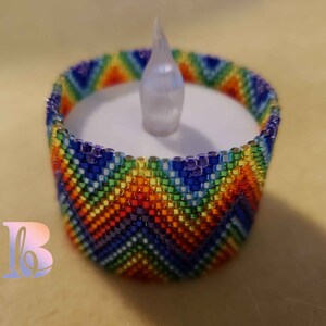 May include: A rainbow beaded candle holder with a white LED tea light inside. The holder is made of small, colorful beads in a chevron pattern.