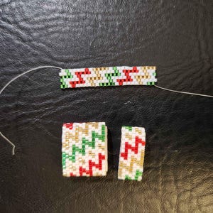 May include: Beaded jewelry components in red, green, gold, and white. The components include a bracelet and two smaller rectangular pieces, all with a zig-zag pattern. The beads are strung on a white thread, and the background is a dark surface.