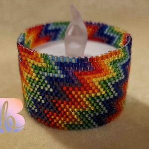 May include: A rainbow beaded candle holder with a white LED tea light inside. The holder is made of small, colorful beads that are woven together in a pattern.