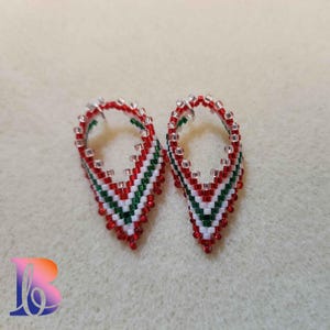May include: A pair of teardrop-shaped earrings. The earrings are hand-beaded with red, white, and green beads in a chevron pattern. The top of the earrings are lined with clear beads. The earrings are displayed on a neutral background.