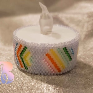 May include: A white LED tea light candle with a beaded band featuring a colorful rainbow chevron pattern. The candle has a flickering flame effect and is designed for decorative use.