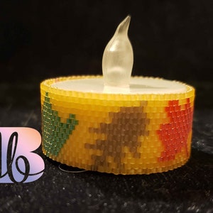May include: A beaded candle holder with a yellow, red, green, and brown pattern. The candle holder is designed to hold a small tea light candle.