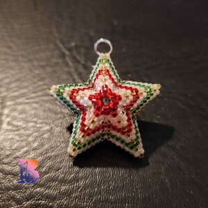 May include: A beaded star ornament with a red, white, and green color scheme. The star is made of small beads and has a metallic silver loop for hanging.