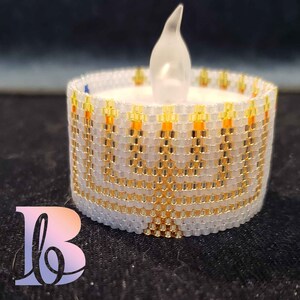 May include: A white beaded candle holder with a gold and orange design. The candle holder is shaped like a menorah and has a small LED tea light inside.