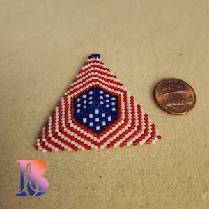 May include: A triangular beaded ornament with a red, white, and blue design, resembling the American flag. The ornament is next to a United States one-cent coin. The ornament is approximately 1.5 inches wide.