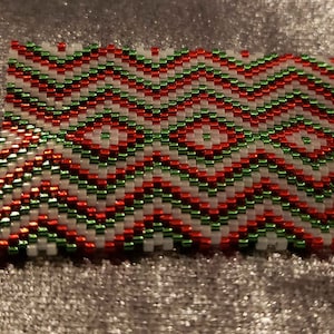 May include: A close-up of a red, green, and white beaded chevron pattern. The beads are small and create a wavy, zig-zag design.