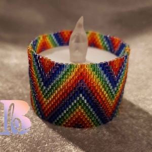 Puede incluir: Un portavelas de cuentas de arcoíris con una vela LED blanca dentro. El portavelas está hecho de pequeñas cuentas de colores dispuestas en un patrón de chevron.