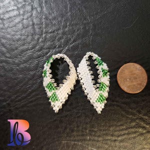 May include: A pair of white and green beaded earrings with a teardrop shape. The earrings are small and delicate, and they are perfect for adding a touch of color to any outfit.