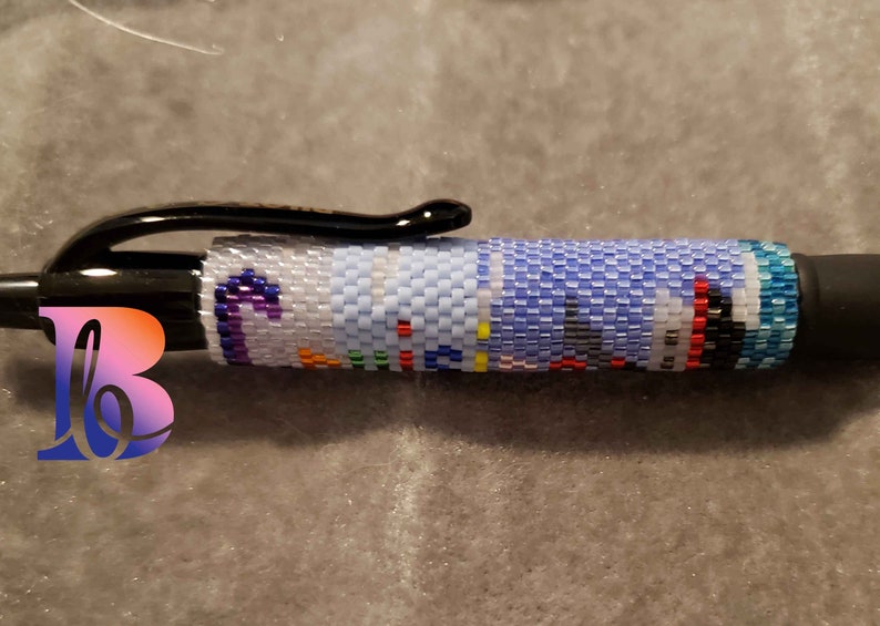 Puede incluir: Un bol&iacute;grafo negro con un dise&ntilde;o de cuentas de colores. Las cuentas est&aacute;n dispuestas en un patr&oacute;n que se asemeja a un paisaje urbano. El bol&iacute;grafo mide aproximadamente 12,5 cm de largo.