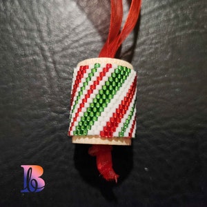 Peut inclure: Une petite décoration de Noël en bois avec un motif de canne en sucre rouge, blanc et vert. L'ornement est attaché à un ruban rouge.