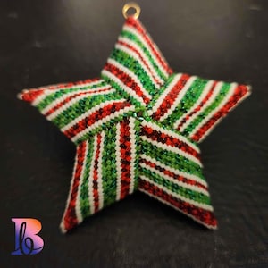 May include: A beaded star ornament in red, green, and white stripes. The star has a gold loop for hanging. The ornament is likely handmade and suitable for holiday or Christmas decor.
