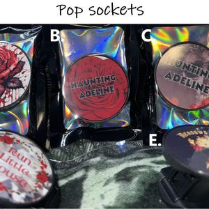 Puede incluir: Cuatro dise&ntilde;os diferentes de popsockets. El primero es una rosa roja con salpicaduras de sangre, el segundo es una rosa roja con el texto "Haunting Adeline", el tercero es una imagen en blanco y negro con el texto "Hunting Adeline", y el cuarto es una imagen en blanco y negro con el texto "Run Little Mouse".