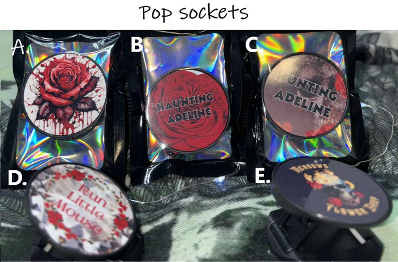 Puede incluir: Cuatro dise&ntilde;os diferentes de popsockets. El primero es una rosa roja con salpicaduras de sangre, el segundo es una rosa roja con el texto "Haunting Adeline", el tercero es una imagen en blanco y negro con el texto "Hunting Adeline", y el cuarto es una imagen en blanco y negro con el texto "Run Little Mouse".