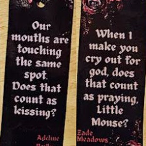 May include: Two black bookmarks with red floral designs and white text. The first bookmark reads "Our mouths are touching the same spot. Does that count as kissing? Adeline Reilly". The second bookmark reads "When I make you cry out for god, does that count as praying, Little Mouse? Zade Meadows".