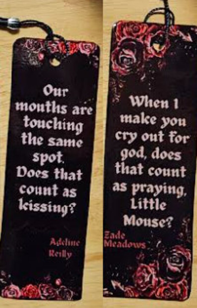 May include: Two black bookmarks with red floral designs and white text. The first bookmark reads "Our mouths are touching the same spot. Does that count as kissing? Adeline Reilly". The second bookmark reads "When I make you cry out for god, does that count as praying, Little Mouse? Zade Meadows".