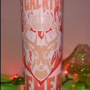 Puede incluir: Un vaso blanco con un diseño rojo y naranja que presenta un ciervo con cuernos, una corona y el texto "Gálatas 4:4". El texto "And light and ask and she bowed for" está en la parte inferior del vaso.