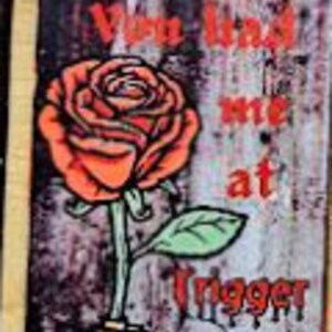 May include: A bookmark with a grunge background featuring a red rose with a gun behind it. The text reads "You find me at Trigger Warning".