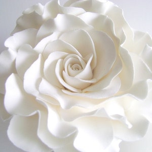 May include: A large, white, fondant rose with ruffled petals. The rose is a cake topper or decoration.
