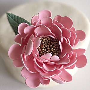 May include: A pink sugar flower with gold sprinkles in the center. The flower is made of fondant and is perfect for decorating cakes and cupcakes.