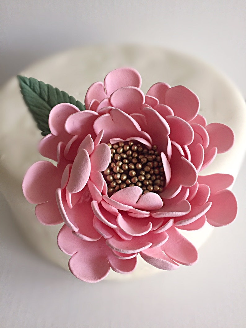May include: A pink sugar flower with gold sprinkles in the center. The flower is made of fondant and is perfect for decorating cakes and cupcakes.