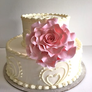 May include: Two-tiered white wedding cake decorated with delicate white frosting and a large pink fondant rose.