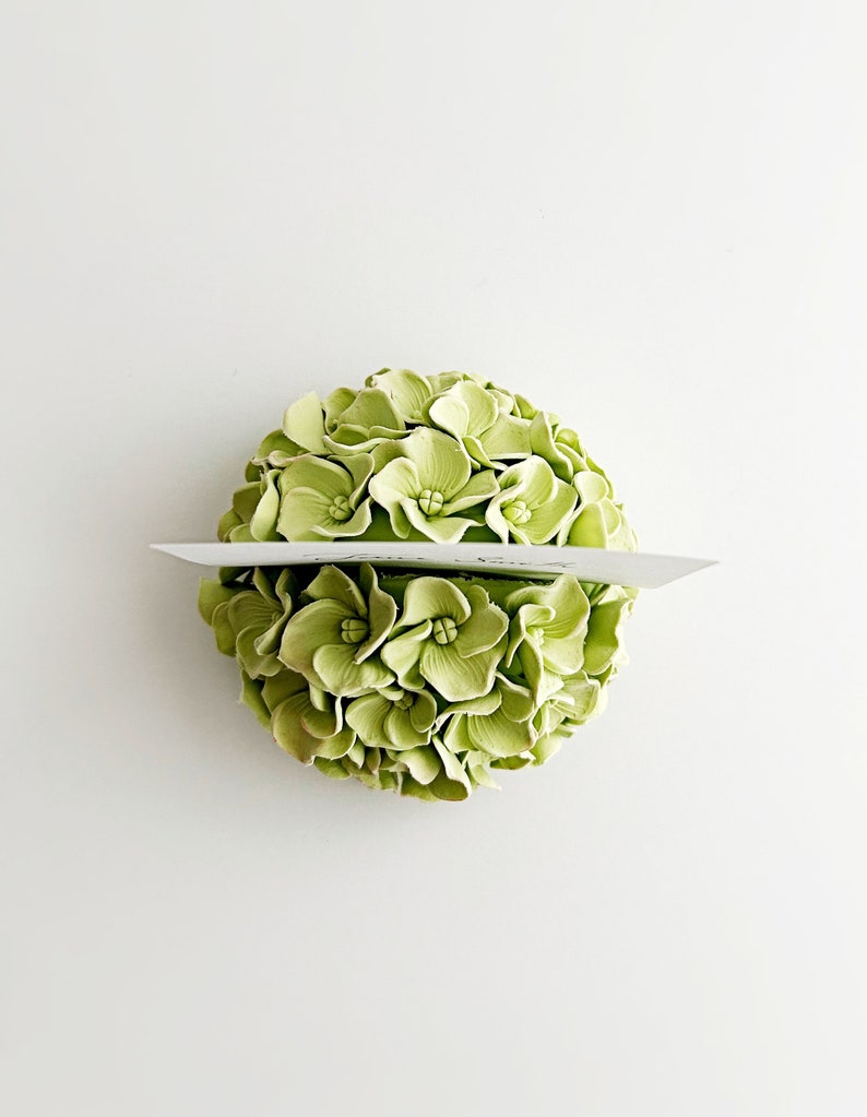 Puede incluir: Un arreglo floral de hortensias verdes con una tarjeta en blanco para un porta nombres.
