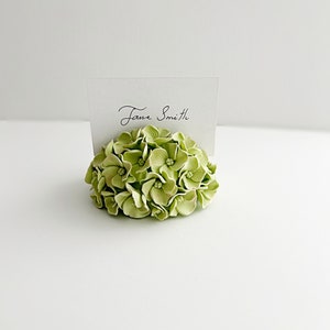 Puede incluir: Un porta tarjetas de lugar de flores de hortensia verde con una tarjeta blanca que dice "Jane Smith".