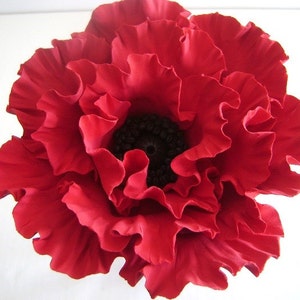 May include: A large, red, fabric poppy flower with a black center. The flower is made of many layers of fabric petals.