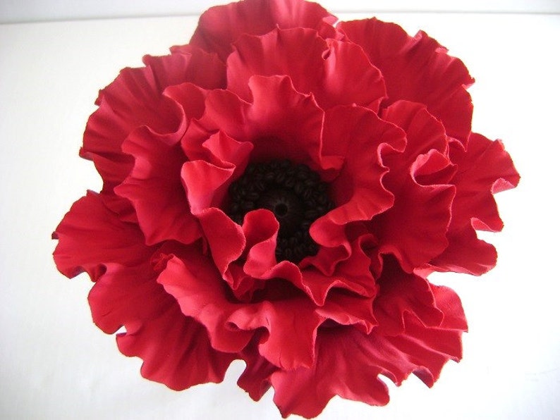 May include: A large, red, fabric poppy flower with a black center. The flower is made of many layers of fabric petals.