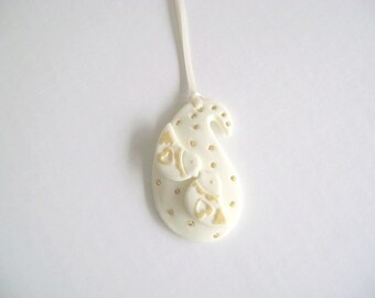 Op de afbeelding: Witte porseleinen hanger in paisleyvorm met gouden accenten. De hanger heeft een ontwerp met harten en krulvormen.