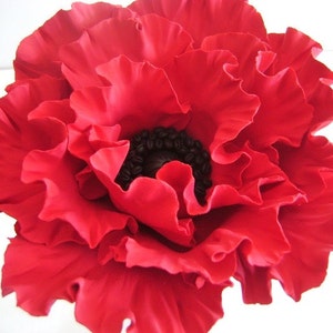 May include: A large, red poppy flower with a black center. The flower is made of fabric and has a ruffled texture.