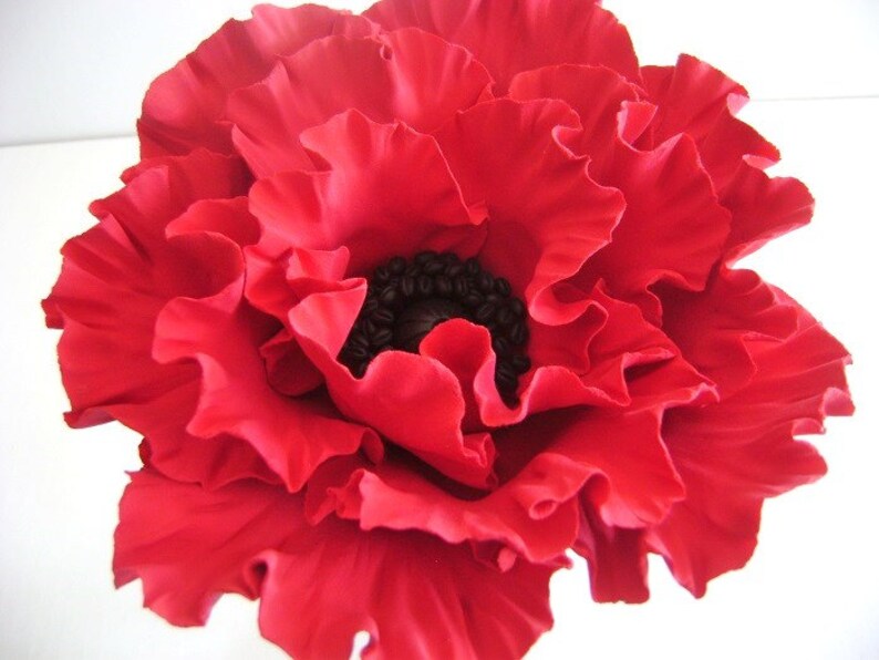 May include: A large, red poppy flower with a black center. The flower is made of fabric and has a ruffled texture.