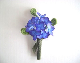 May include: A small bouquet of blue and purple flowers with green leaves. The flowers are arranged in a cluster and tied together with a green ribbon.
