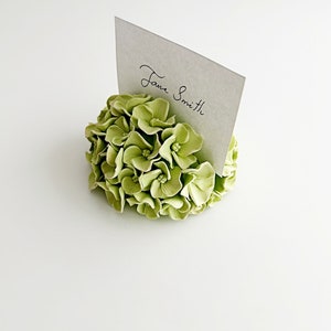 Puede incluir: Un porta tarjetas de lugar floral verde con una tarjeta blanca que dice "Jane Smith".