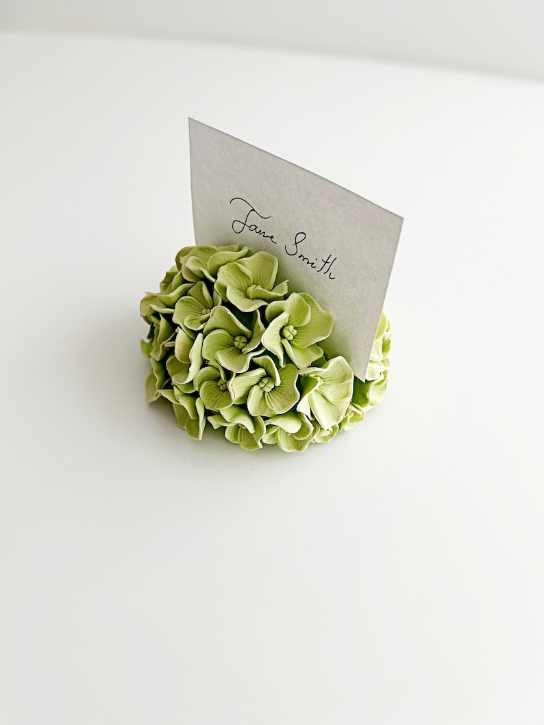 Puede incluir: Un porta tarjetas de lugar floral verde con una tarjeta blanca que dice "Jane Smith".