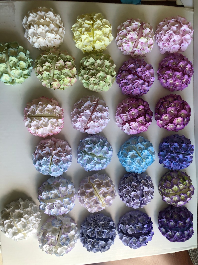 Puede incluir: Una colecci&oacute;n de 25 arreglos redondos de flores de hortensia en varios tonos de azul, morado, verde y blanco. Las flores est&aacute;n dispuestas en un patr&oacute;n circular y todas son del mismo tama&ntilde;o.