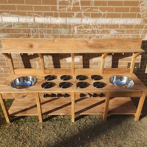 K&ouml;nnte beinhalten: Eine h&ouml;lzerne Spielk&uuml;che mit zwei Edelstahlsp&uuml;len, sechs schwarzen Herdplatten und zwei Regalen. Die K&uuml;che ist aus Naturholz gefertigt und hat einen rustikalen Look.