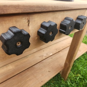 K&ouml;nnte beinhalten: Eine Holzk&uuml;che zum Spielen mit schwarzen Plastikkn&ouml;pfen und einem schwarzen Kochfeld. Die K&uuml;che ist aus unbehandeltem Holz und hat ein Regal darunter.