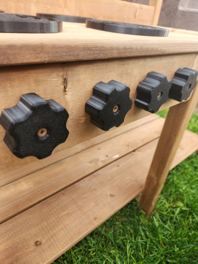 K&ouml;nnte beinhalten: Eine Holzk&uuml;che zum Spielen mit schwarzen Plastikkn&ouml;pfen und einem schwarzen Kochfeld. Die K&uuml;che ist aus unbehandeltem Holz und hat ein Regal darunter.