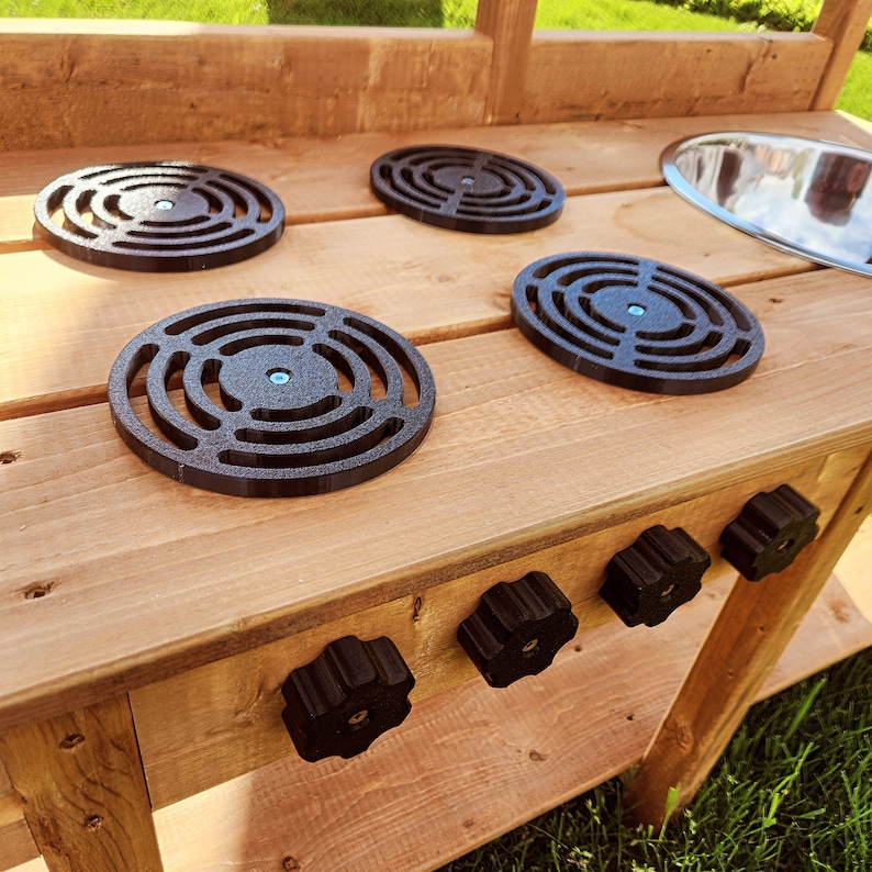 K&ouml;nnte beinhalten: Holzspielk&uuml;che mit vier schwarzen Herdplattenkn&ouml;pfen und vier schwarzen Herdplattenabdeckungen. Die K&uuml;che hat ein Edelstahlsp&uuml;lbecken und vier schwarze Kn&ouml;pfe zum Einschalten des Herdes.
