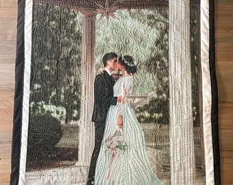 May include: A wedding quilt with a photo of a couple kissing under a pergola. The quilt is white with black trim and has the names "Aerin & Nate Stamp" and the date "9.10.22" embroidered on it.