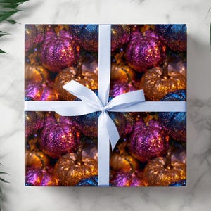 May include: A wrapped gift with a white ribbon. The wrapping paper features a pattern of glittery pumpkins in shades of purple, gold, and blue. The gift is presented on a white marble surface, with green leaves in the background.