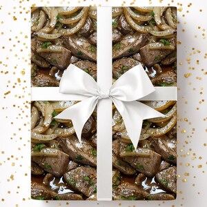 May include: Gift wrap featuring a pattern of cooked meat and onions, tied with a white satin ribbon and bow. The wrapping paper design shows a close-up of the food, with a white background and gold confetti.