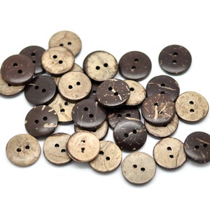 May include: A collection of round, two-hole buttons in varying shades of brown and tan. The buttons appear to be made of natural material, possibly coconut shell, with visible grain and texture. The buttons are scattered on a white background.