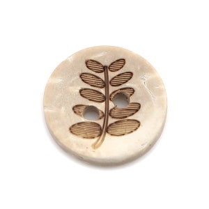 May include: A white button with a brown leaf design. The button has two holes.