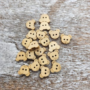 May include: A collection of wooden bear-shaped buttons in a light brown color. The buttons are scattered on a light brown wooden surface.