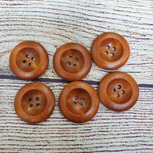 May include: Six brown wooden buttons with four holes each. The buttons are arranged in two rows of three.
